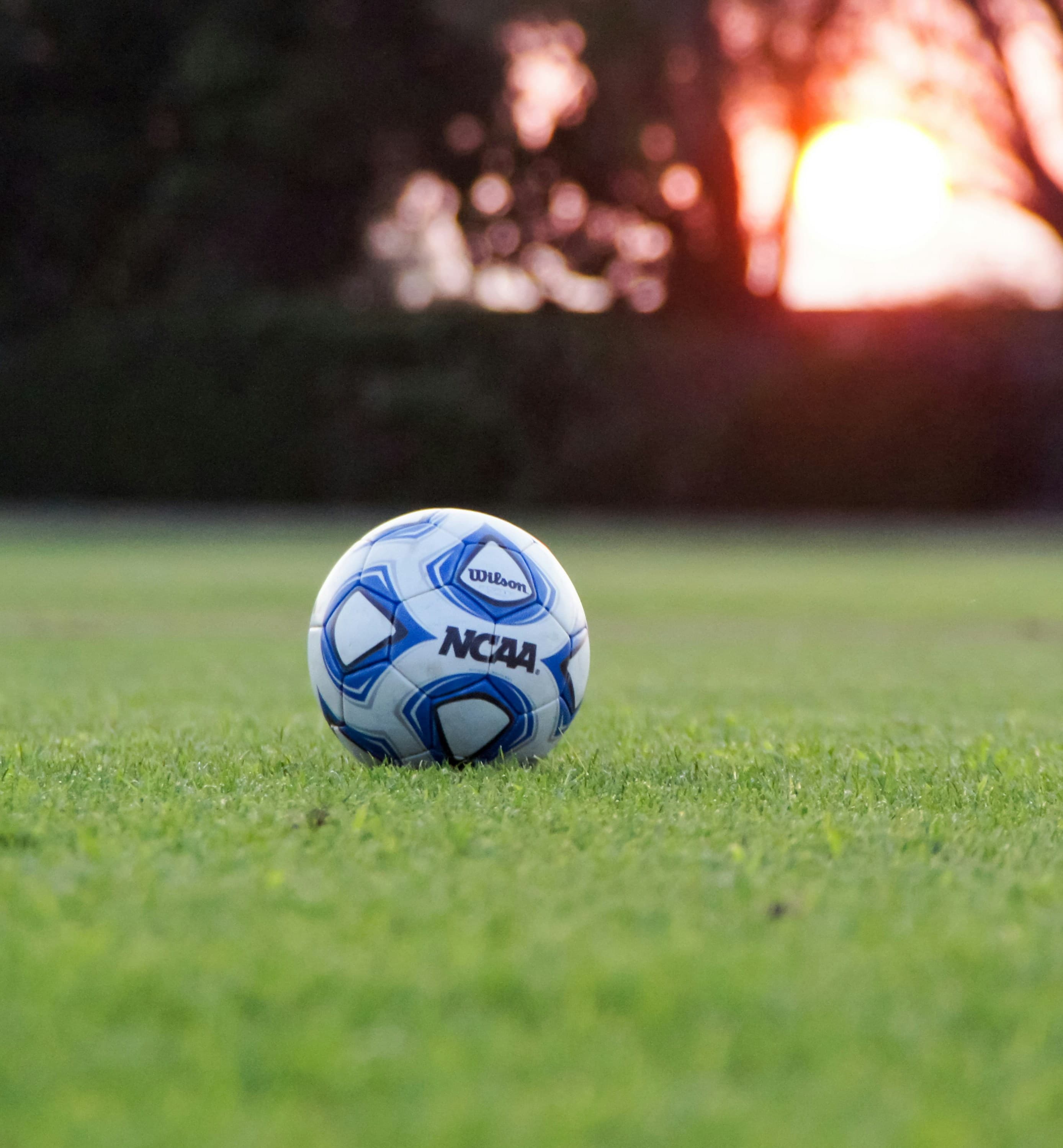NCAA soccer ball on grass field during stadium evening lighting