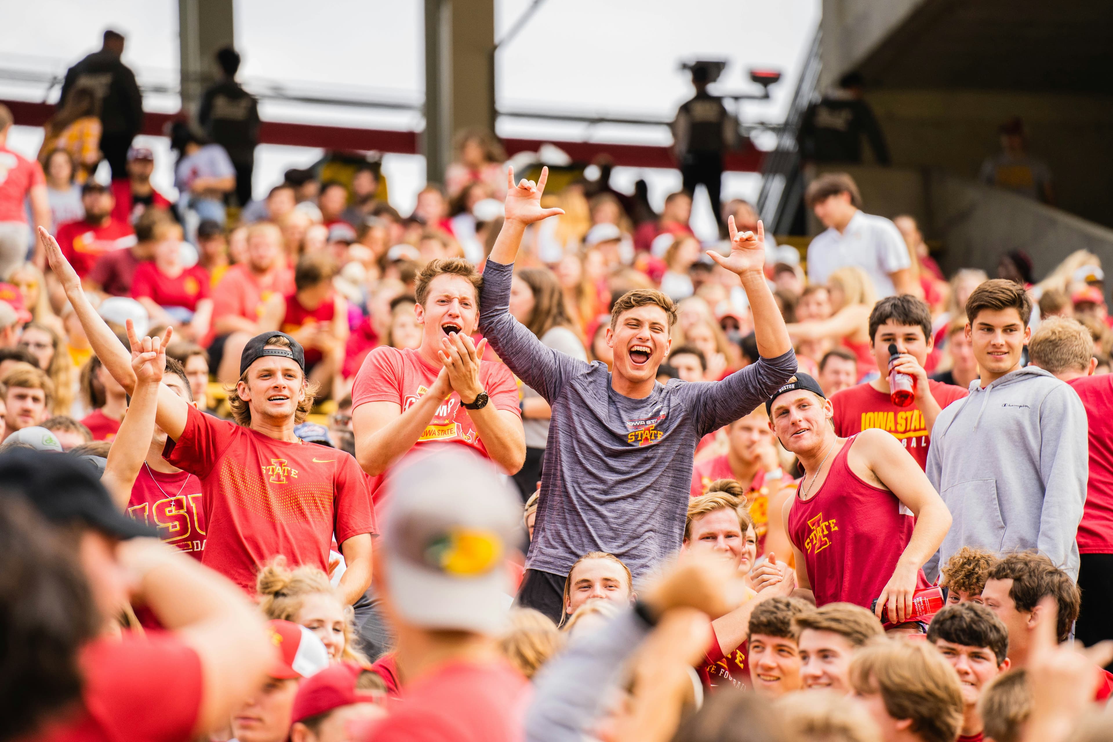A large crowd of enthusiastic collegiate fans in red and gray gear cheering in a stadium during a game.