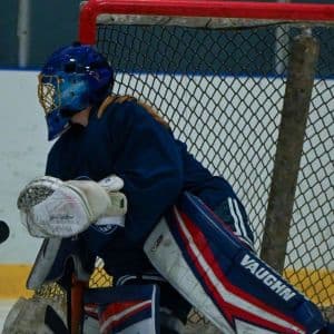 An ice hockey goalkeeper in blue and red guarding the goal.