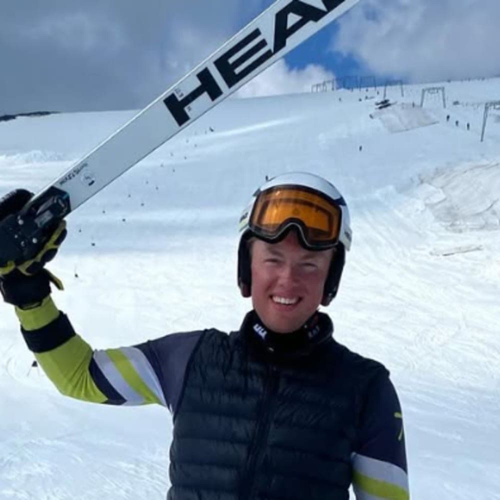 Bosse Mikelsson – Montana State University, NCAA DI A young male skier holding his skis above his head and smiling on a skiing slope.