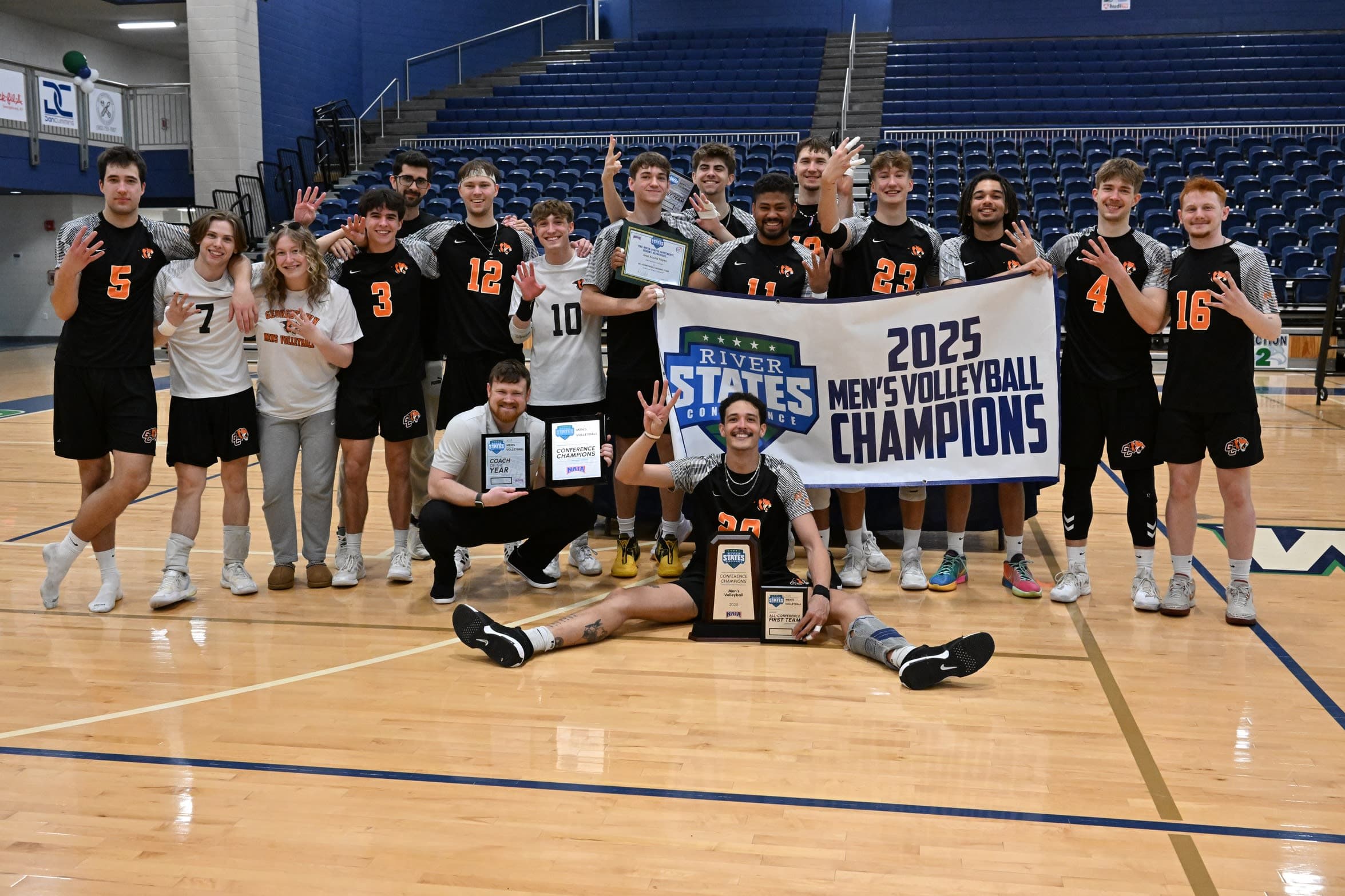 College Volleyball Team Celebrating Championship | Smarthlete College volleyball team celebrating a championship with a banner and trophy.
