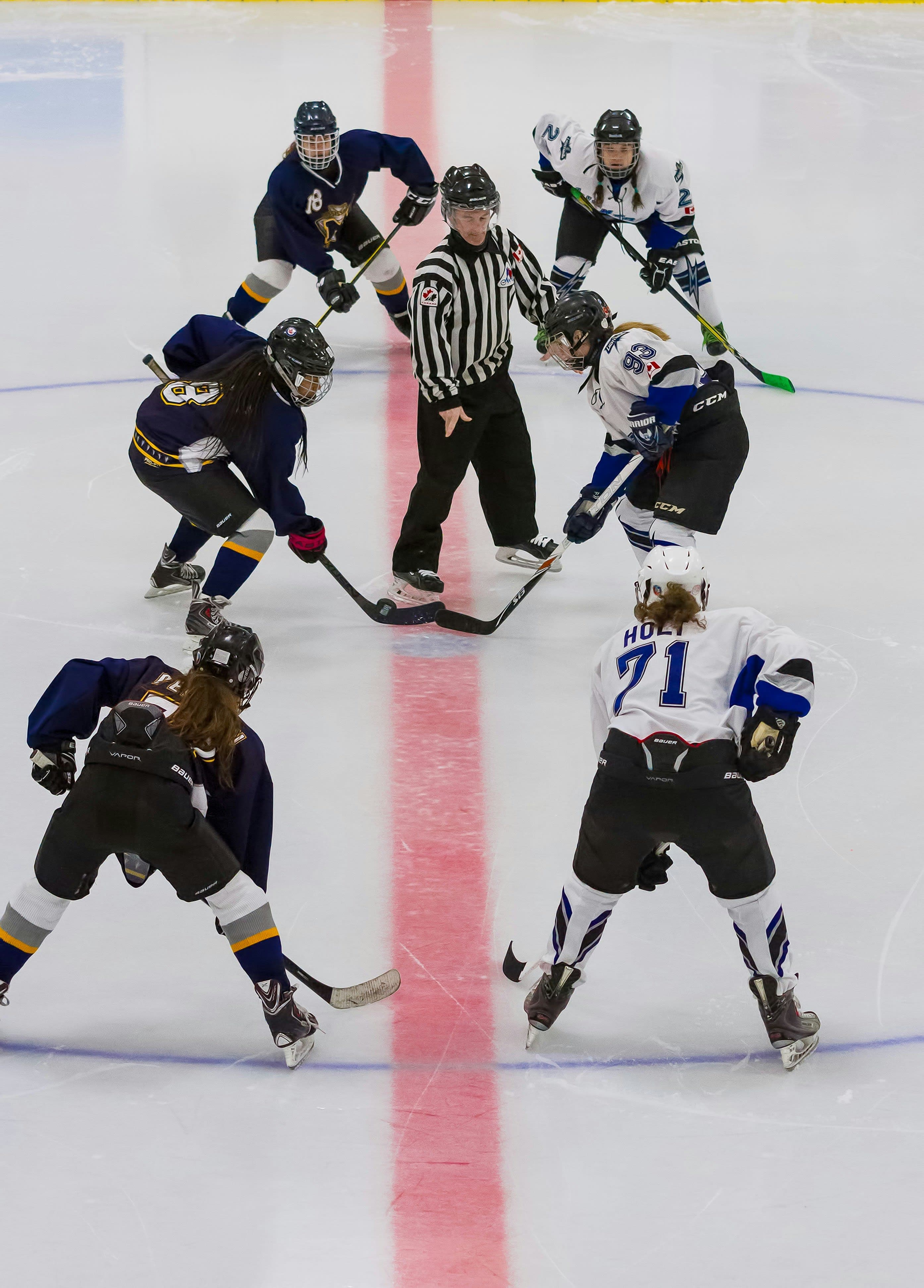 Female College Ice Hockey Face-Off | NCAA Game Two female ice hockey players prepare for a face-off as the referee is about to drop the puck during a game.