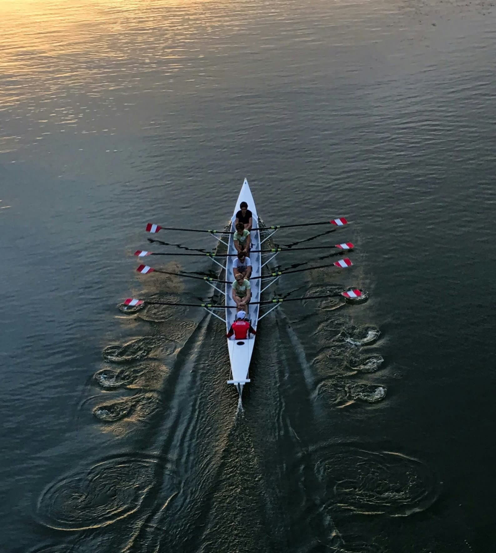 Aerial View of College Rowing Shell at Sunset | Smarthlete Aerial view of a rowing shell with a coxswain and four rowers gliding across calm water during the sunset.