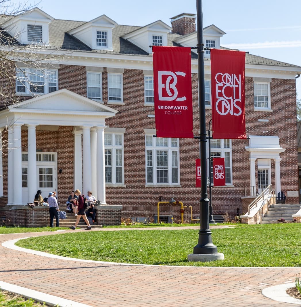 Bridgewater College campus building with red banners and students walking on campus quad