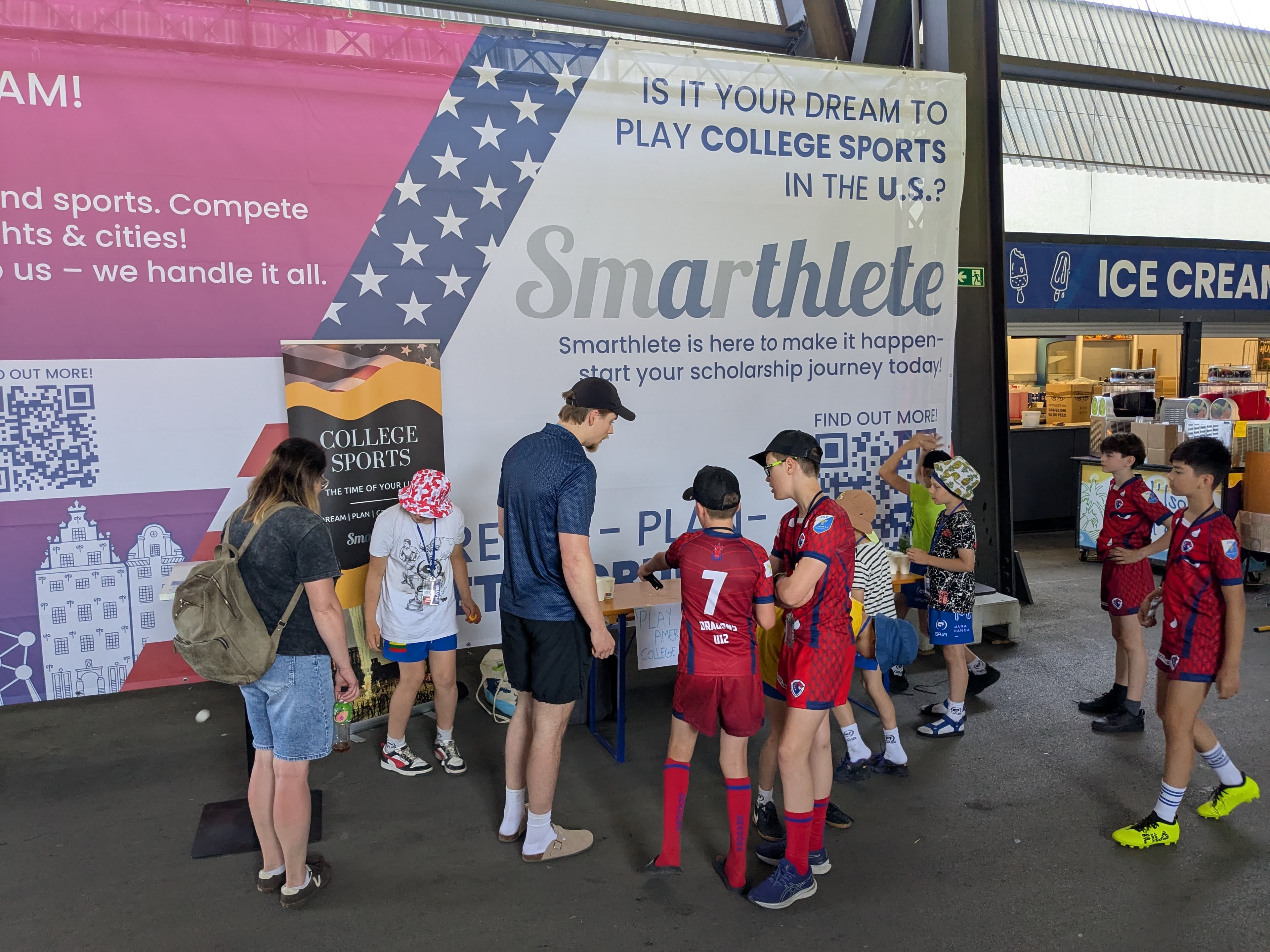 Smarthlete Information Stand at the United World Games A large Smarthlete promotional banner at an information stand asking 'Is it your dream to play college sports in the U.S.?' with young athletes in front of it.