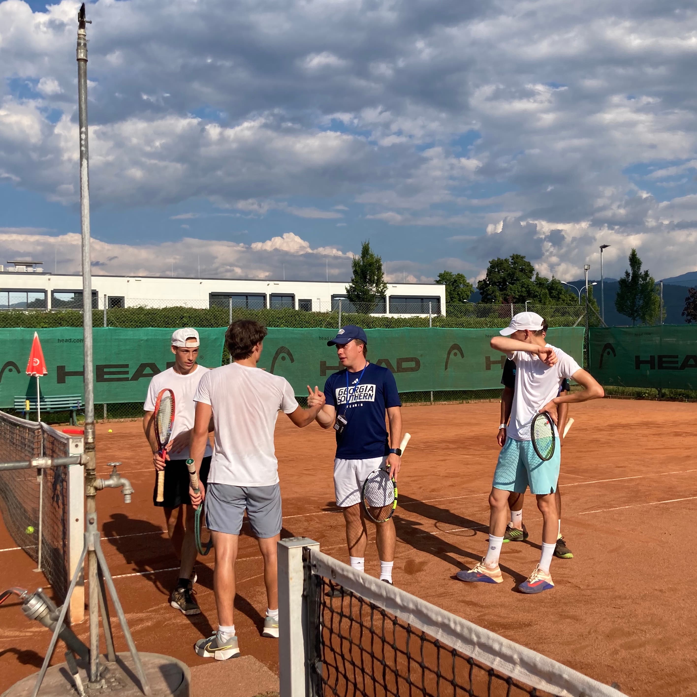 College Tennis Coach Meeting Student-Athlete at the Smarthlete Showcase A college tennis coach in a navy shirt shaking hands with a student-athlete on a clay court, surrounded by more tennis players.